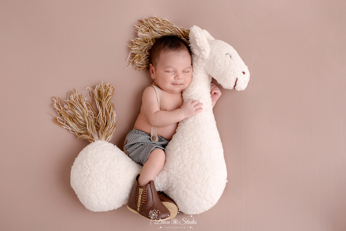 drica studio-ensaio fotografico recém-nascido- newborn-xinguara - pará - bebê recém-nascido dormindo abraçado em cavalinho de pelúcia - bebê veste short com suspensório sem camisa e bota marrom - fundo bege
