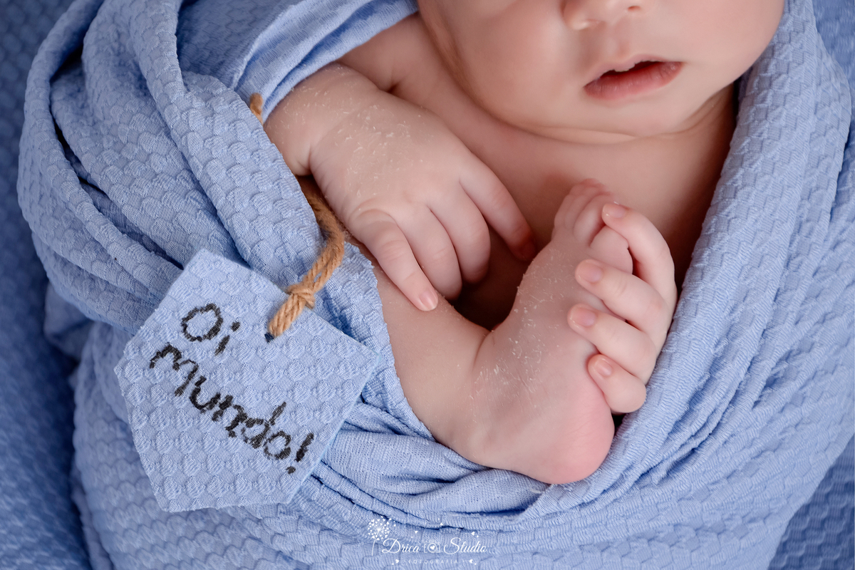 drica studio-ensaio fotografico recém-nascido- newborn-xinguara - pará - bebê recém-nascido enrolado em manta azul, em pose confortável- o bebê segura uma plaquinha escrita 