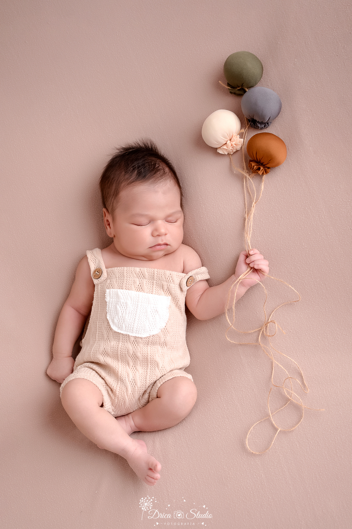 drica studio-ensaio fotografico recém-nascido- newborn-xinguara - pará- bebê recém-nascido dormindo e segurando balões em tons neutros- veste bory bege com bolsinho branco na frente - fundo neutro