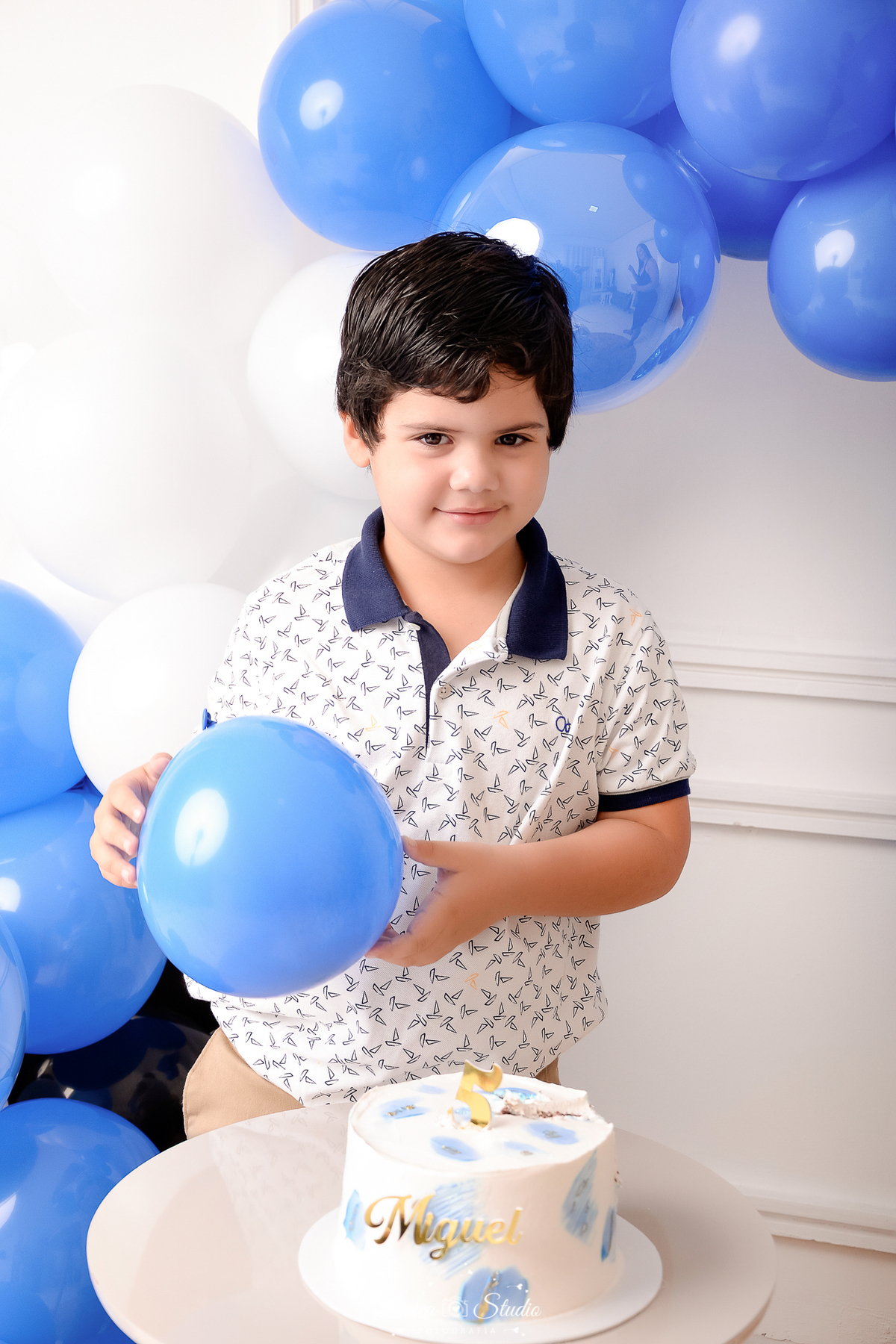 drica studio - ensaio fotografico infantil - 5 anos - xinguara - pará - menino segurando balão azul- camisa gola polo branca com detalhes azuis - fundo branco com boiserie