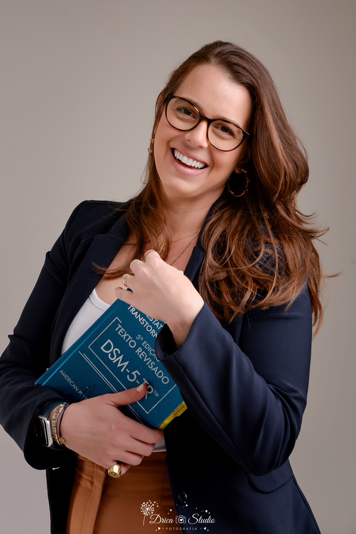 drica studio - ensaio fotografico profissional - psicologia infantil - xinguara - pará- profissional de psicóloga segurando o livro DSM-5-TR, vestindo blazer azul, em ensaio corporativo para psicologia clínica - fundo neutro