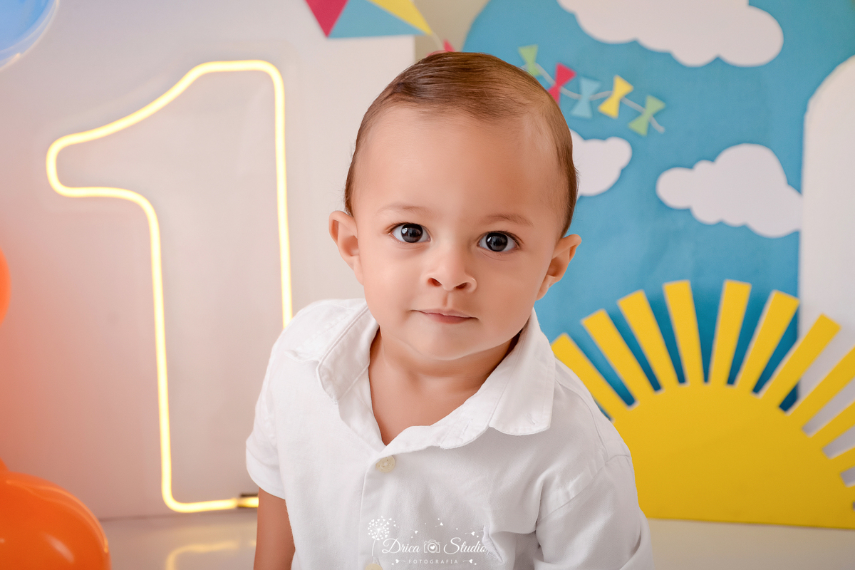 drica studio-ensaio fotografico infantil - xinguara - pará - smash the cake - minha primeira volta ao sol - hum de led - solzinho - nubem- painel azul - pipa colorida- glose em bebê, ele veste camisa branca gola polo branca