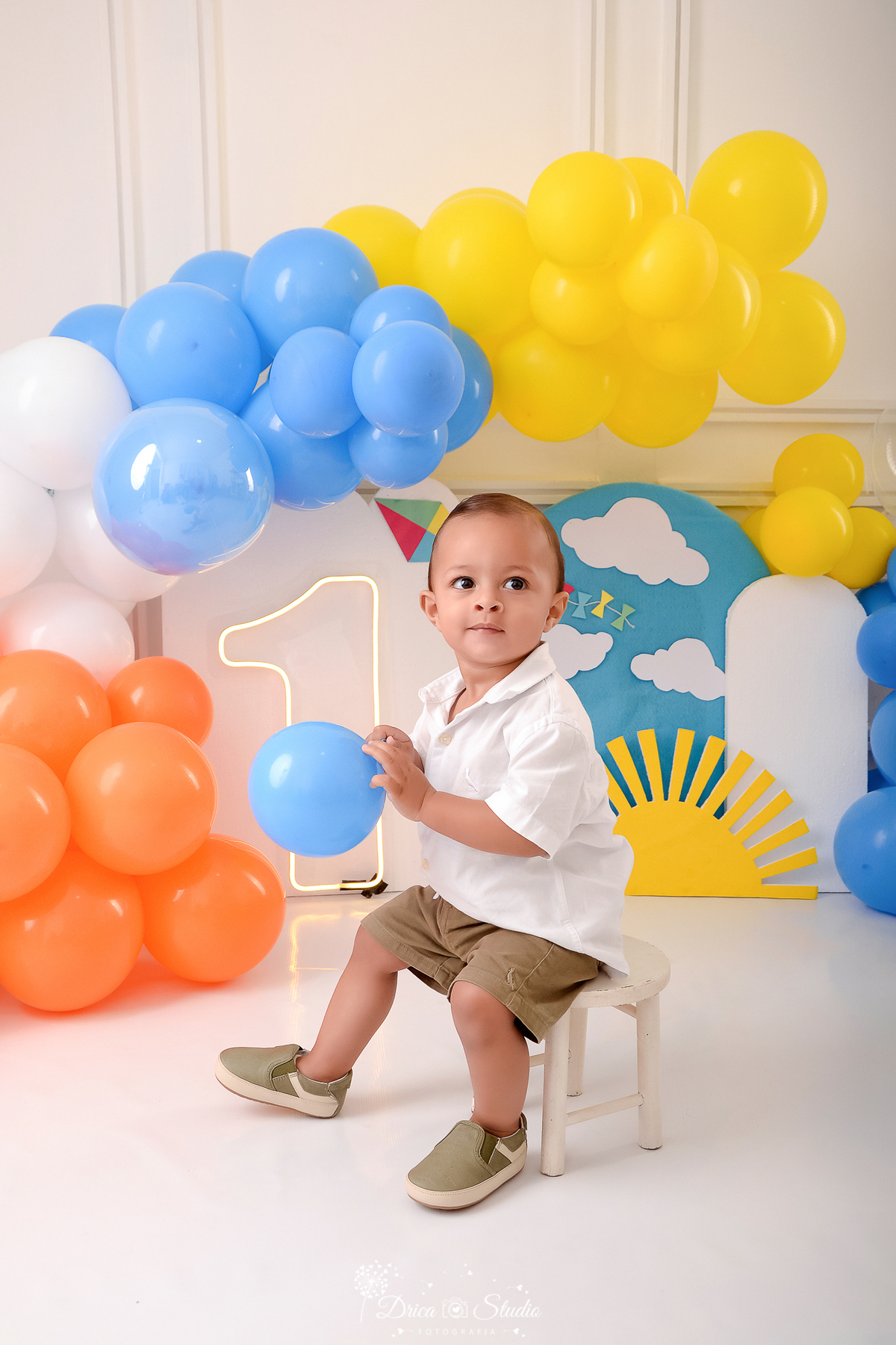 drica studio-ensaio fotografico infantil - xinguara - pará - smash the cake - minha primeira volta ao sol - hum de led - solzinho - baloes laranja, branco, amarelo e azul - bebê sentado em banquinho branco, ele veste camisa branca e short marrom