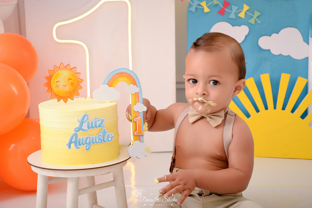 drica studio-ensaio fotografico infantil - xinguara - pará - smash the cake - minha primeira volta ao sol - hum de led - solzinho - bebê sentado no chão degustando bolo - balão laranja - fundo azul com nuvens branca- pipa colorida - fundo branco