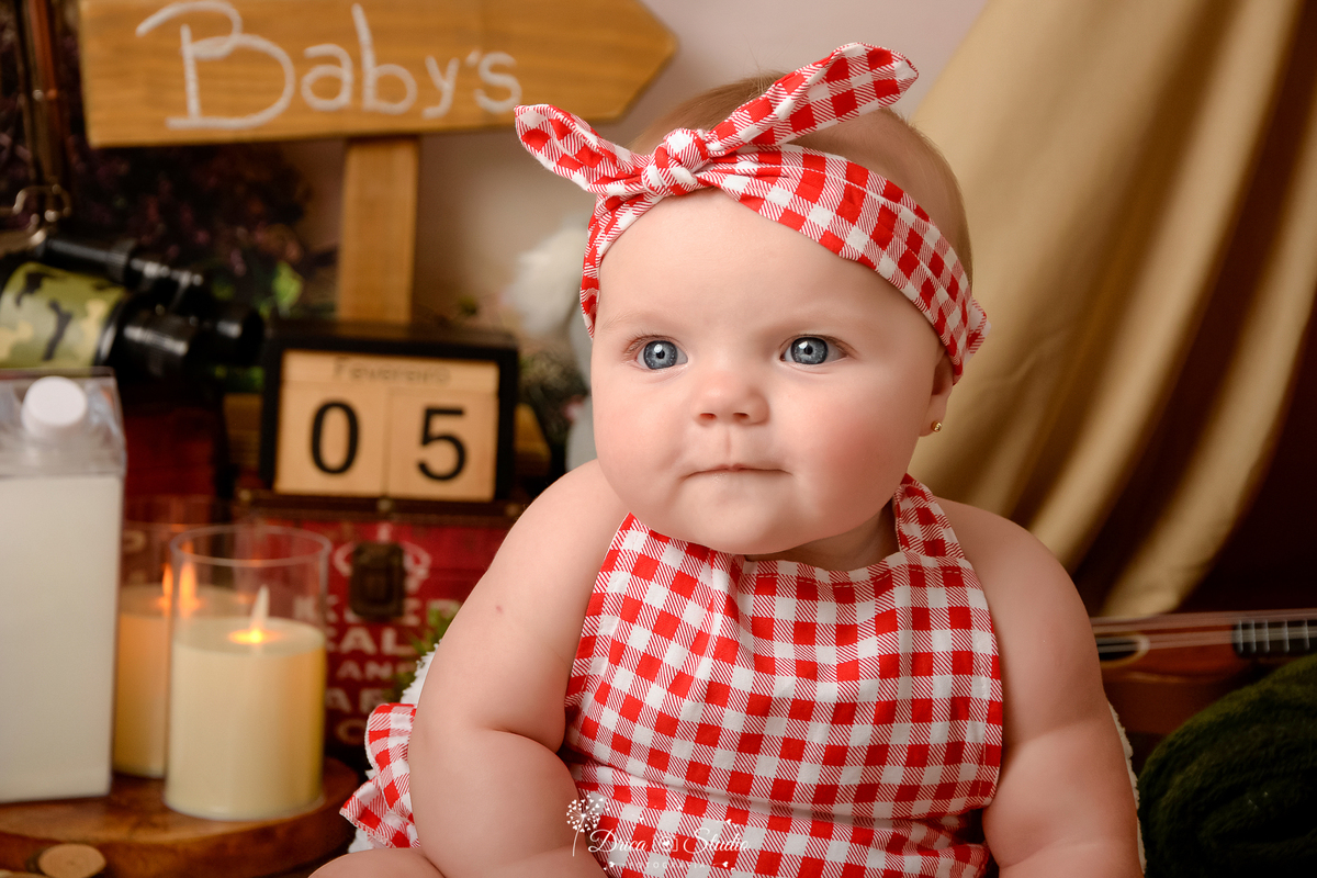 drica studio-ensaio fotografico infantil - acampamento infantil - xinguara - pará -bebê vestida em blusa, shortinho e fita de cabeça xadrez - velas fake - cabaninha - plaquinha de indicação - garrafa de leite 