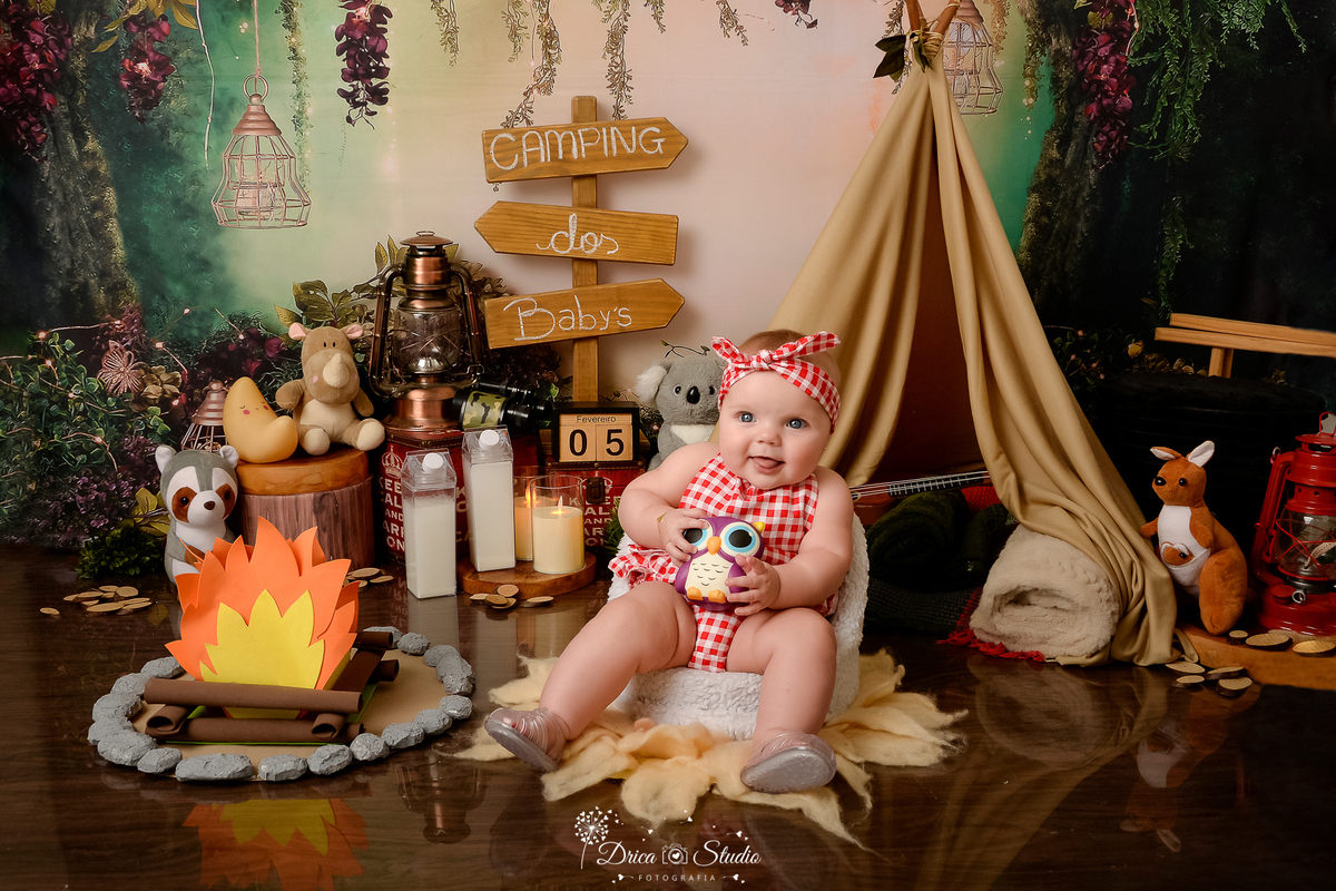 drica studio-ensaio fotografico infantil - acampamento infantil - xinguara - pará -bebê sentada em poltrona branca - veste blusa, short e facha de cabelo xadrez branco com vermelho - lampião - fogueira de eva - fundo tema floresta