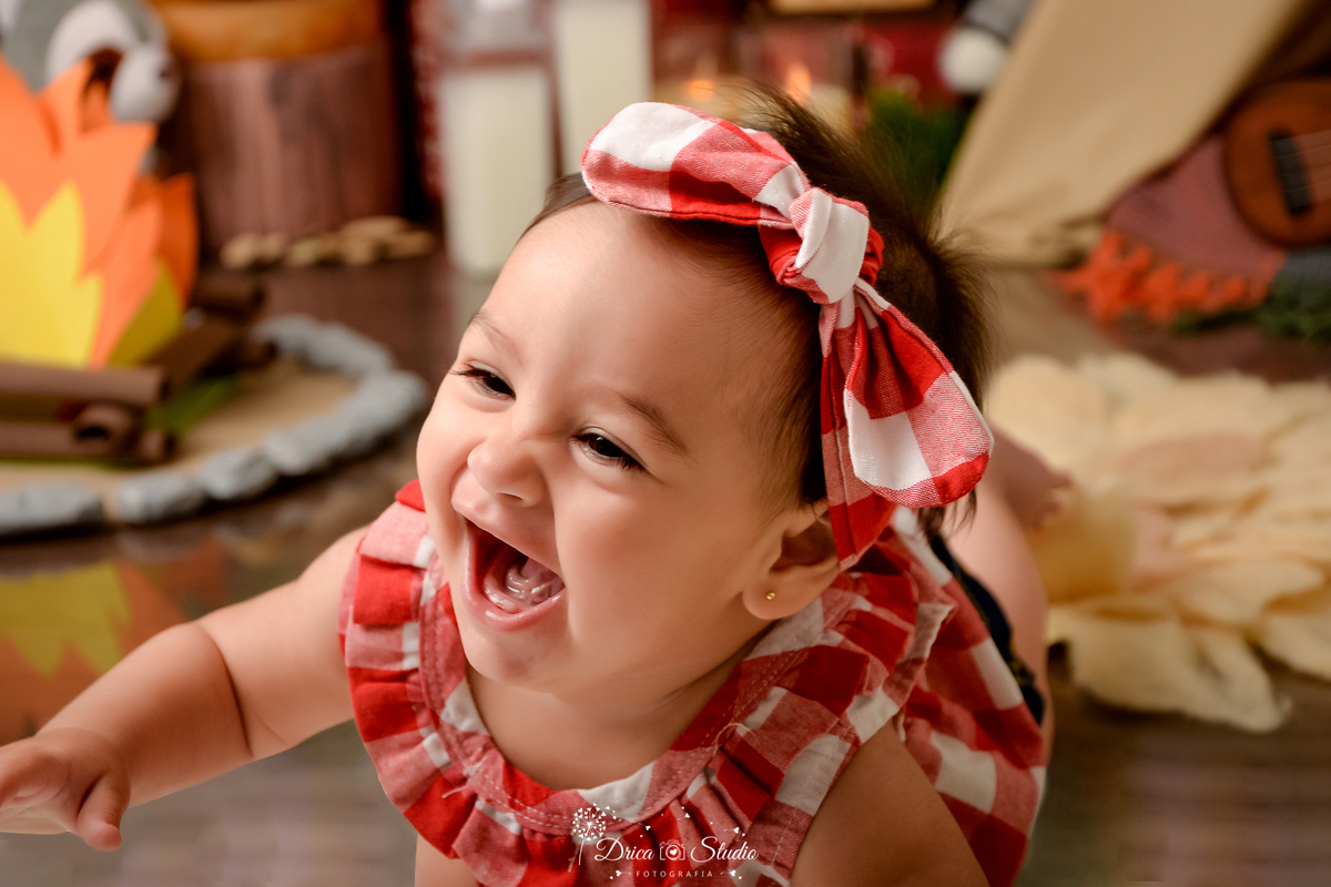 drica studio-ensaio fotografico infantil - acampamento infantil - xinguara - pará - bebê engatiando sorridente, usando blusa xadrez vermelho e branco - tapete felpudo - fogueira de eva - cabaninha - piso amadeirado