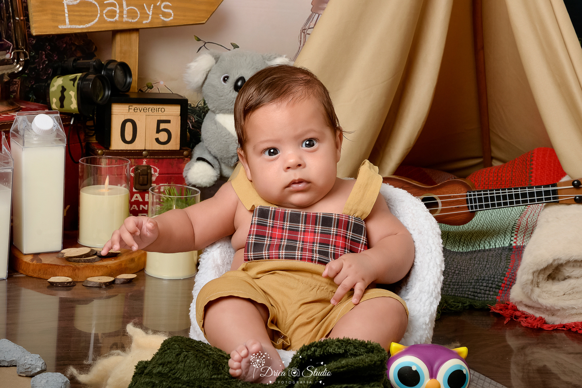 drica studio-ensaio fotografico infantil - acampamento infantil - xinguara - pará - bebê sentada em poltrona branca - cabaninha bege - caixa de leite - vela de led - manta verde escuro - corujinha de brinquedo - fundo tema floresta