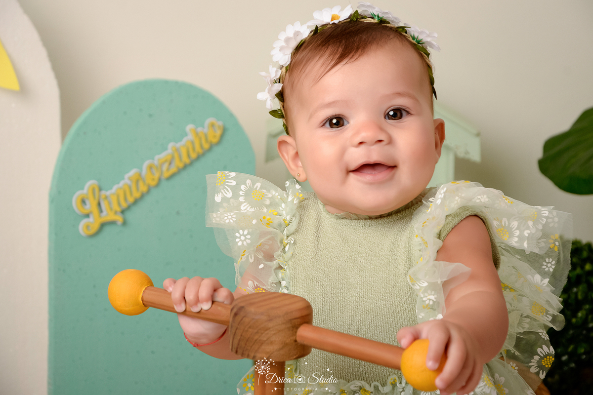 drica studio-ensaio fotográfico infantil - acompanhamento mensal - tema limãozinho -bebê sentada em bicicletinha de madeira com detalhes amarelo - bory verde com mangas de tule branco e aplique de margaridas - tiara de margarida - painel verde