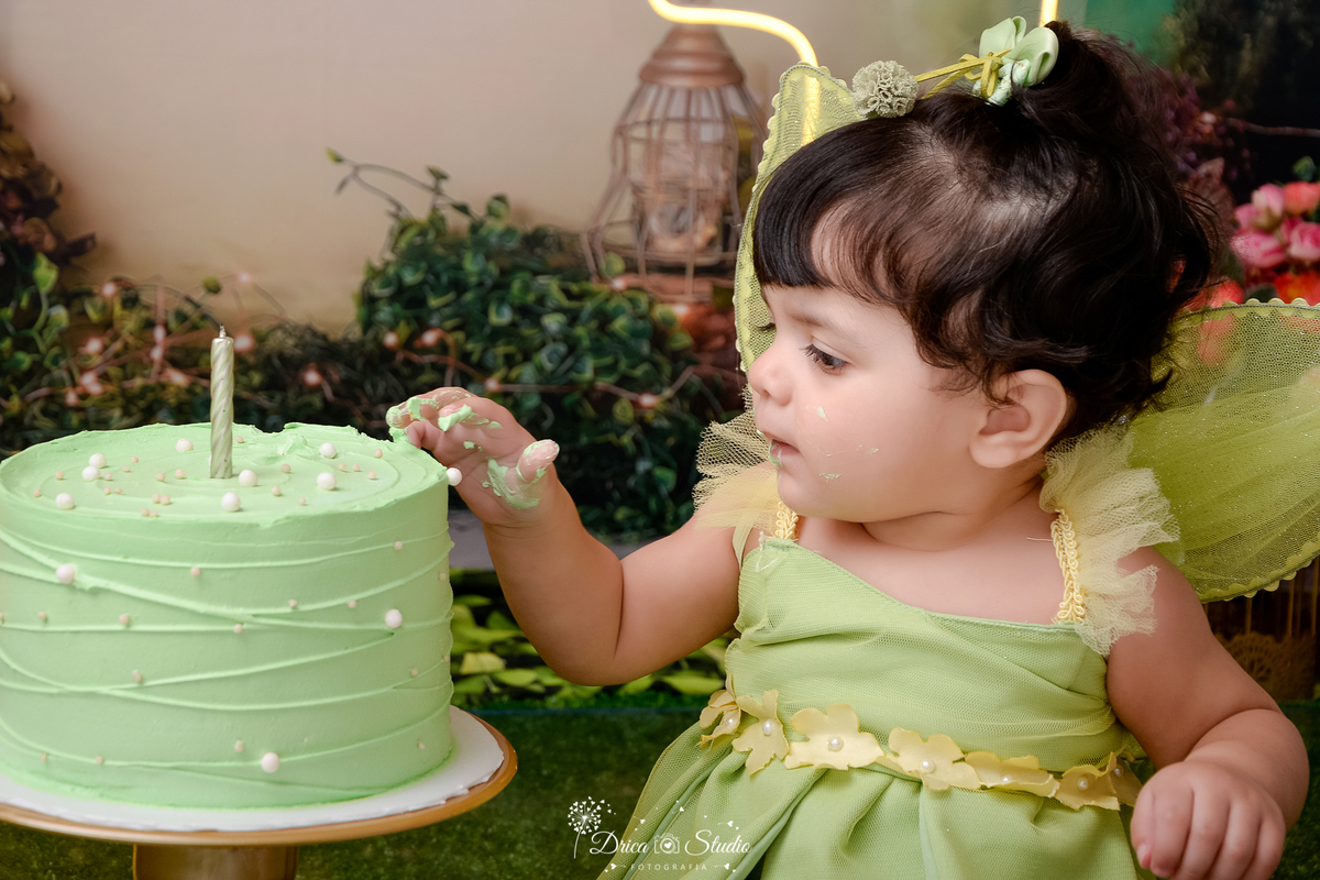 DRICA STUDIO - ENSAIO FOTOGRAFICO INFANTIL - SMASH THE CAKE - TINKER BELL - XINGUARA - BEBÊ SENTADA NO CHÃO TOCANDO EM BOLO - FUNDO TEMA FLORESTA - 