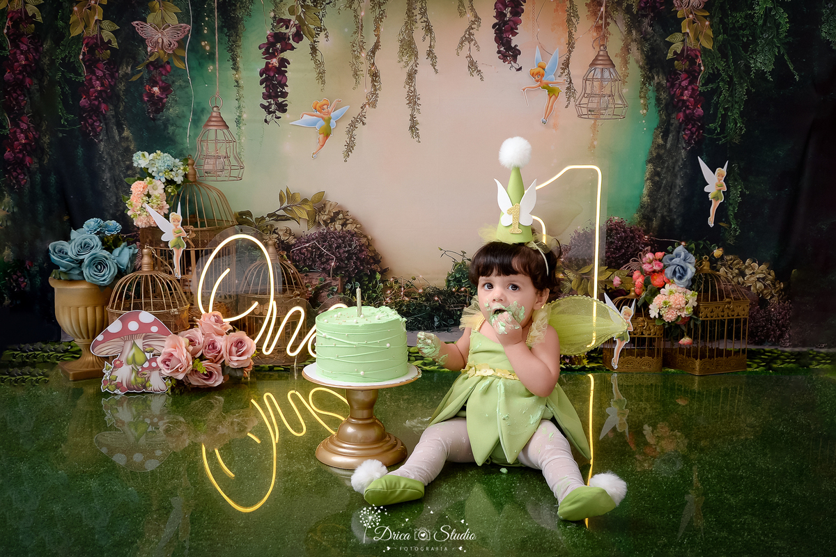 DRICA STUDIO - ENSAIO FOTOGRAFICO INFANTIL - SMASH THE CAKE - TINKER BELL - XINGUARA - BEBÊ SENTADA NO CHÃO DESGUSTANDO BOLO - BOLO VERDE - ONE DE LED - UM DE LED - FUNDO TEMA FLORESTA - CESTO COM FLORES - SININHO