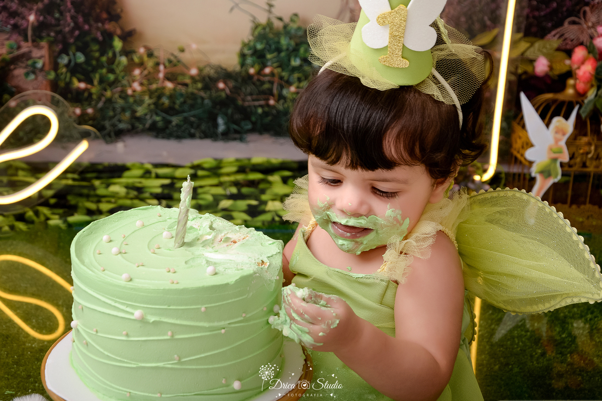DRICA STUDIO - ENSAIO FOTOGRAFICO INFANTIL - SMASH THE CAKE - TINKER BELL - XINGUARA - BEBÊ SENTADA AO LADO DE BOLO NA COR VERDE, VESTIDA DE TINKER BELL - FUNDO TEMA FLORESTA - ONE DE LED - CHAPÉU COM UM DE ACRILICO - FUNDO TEMA FLORESTA