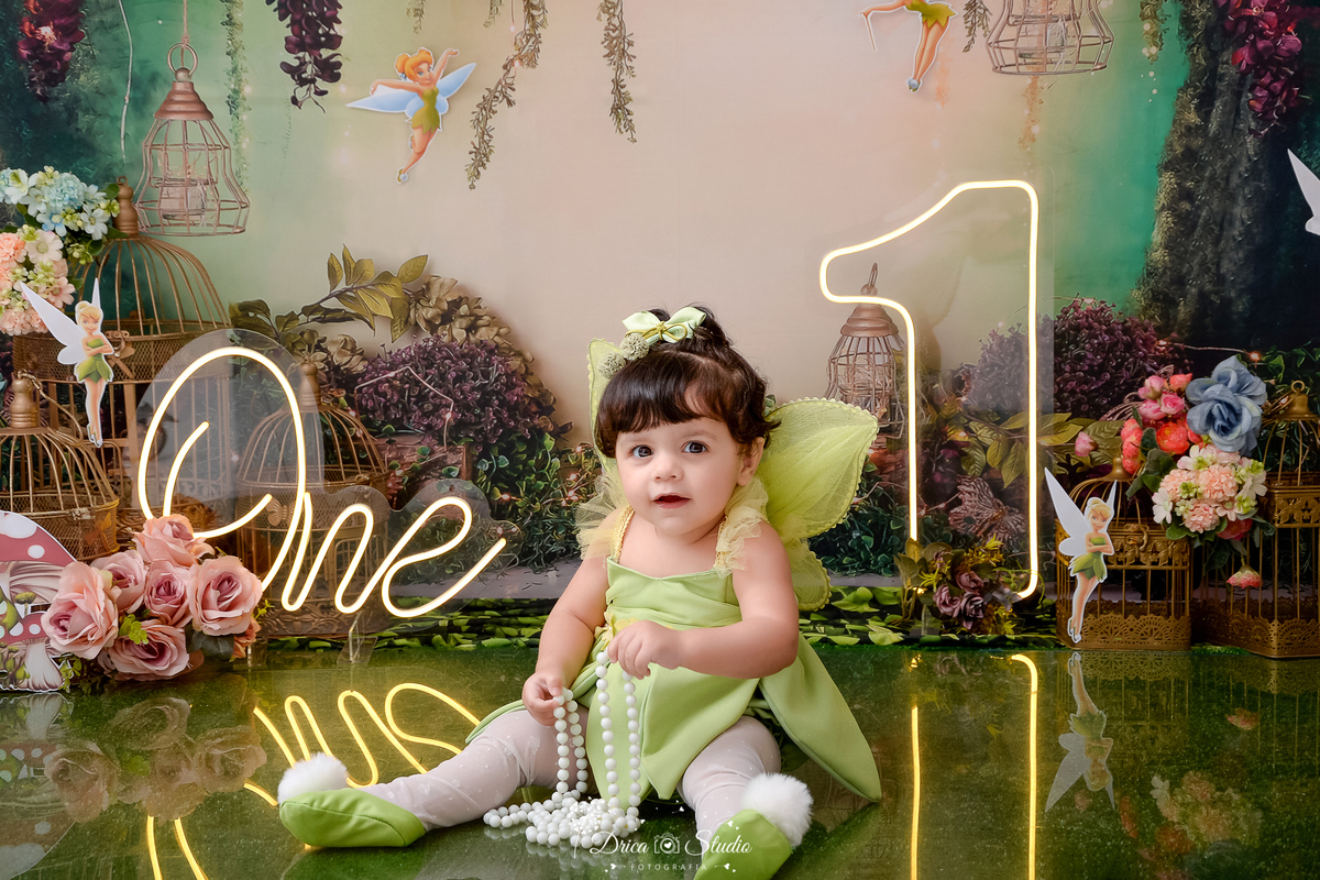 DRICA STUDIO - ENSAIO FOTOGRAFICO INFANTIL - SMASH THE CAKE - TINKER BELL - XINGUARA - BEBÊ VESTIDA DE TINKER BELL SENTADA NO CHÃO SEGURANDO COLAR DE PÉROLA - ONE DE LED - UM DE LED - CESTO COM FLORES - FUNDO TEMA FLORESTA - 