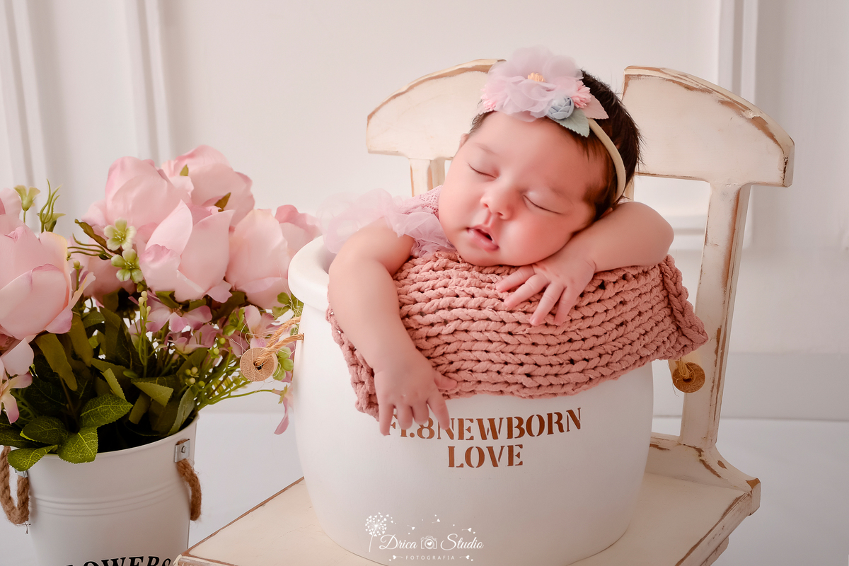 drica studio - ensaio fotografico infantil- recém-nascido- newborn-xinguara-pará-bebê dormindo dentro de cesto de madeira branco, acochoado com manta rose de tricô, sobre cadeira branca de madeira - vaso branco com flores rosa - fundo branco com boiserie 