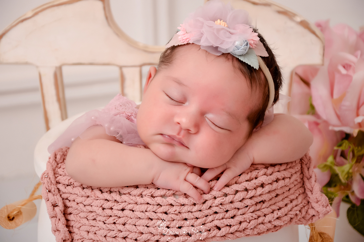 drica studio - ensaio fotografico infantil- recém-nascido- newborn-xinguara-pará-bebê dormindo dentro de cesto acochoado com manta de tricô rose, com laço de flor na cabeça, flores rosa - cadeira de madeira branca - fundo branco com boiserie