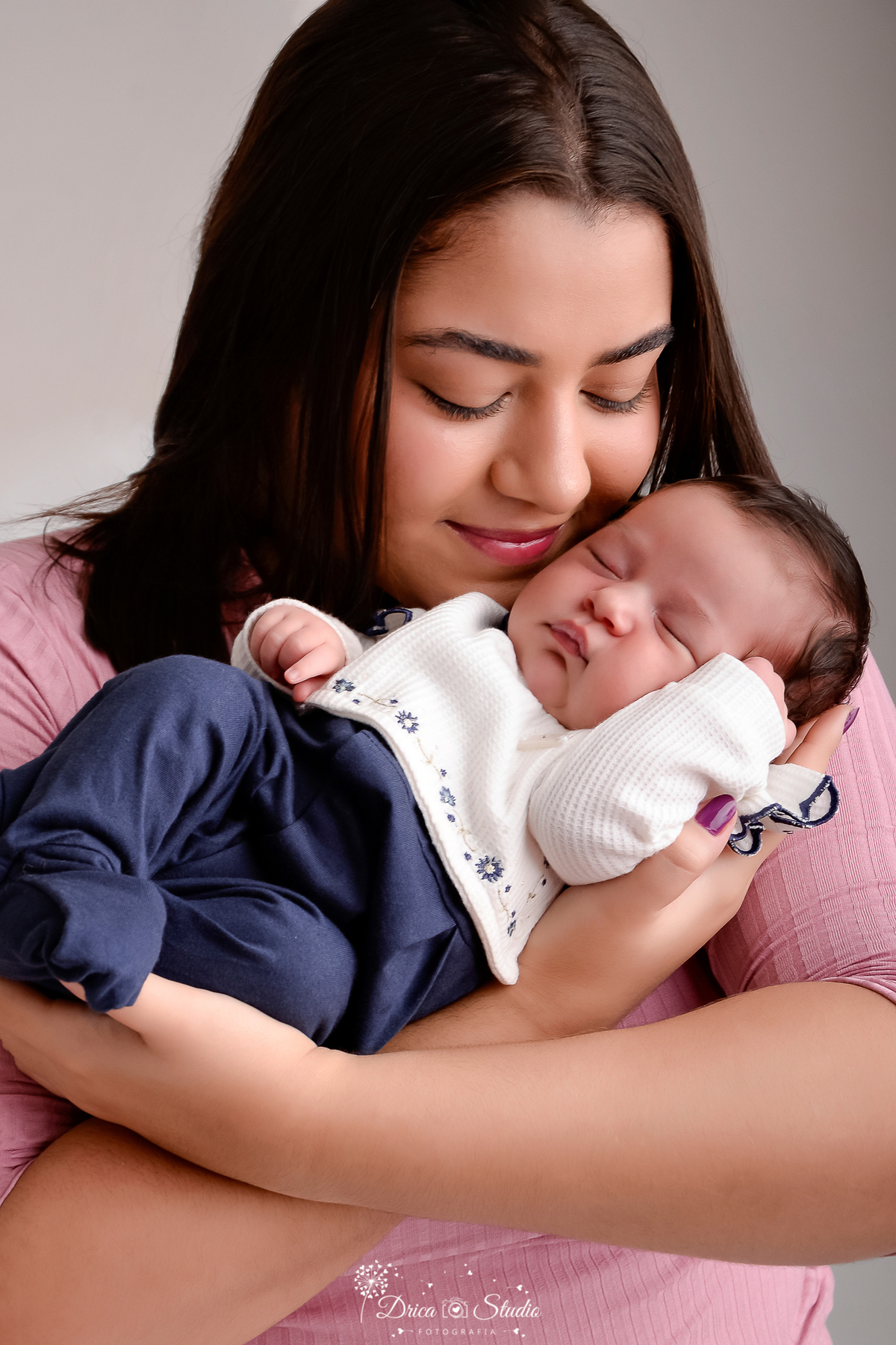 drica studio - ensaio fotografico infantil- recém-nascido- newborn-xinguara-pará-mãe segurando bebê recém-nascido próximo do rosto, a bebê veste pagãzinho azul e blusa de manga branca