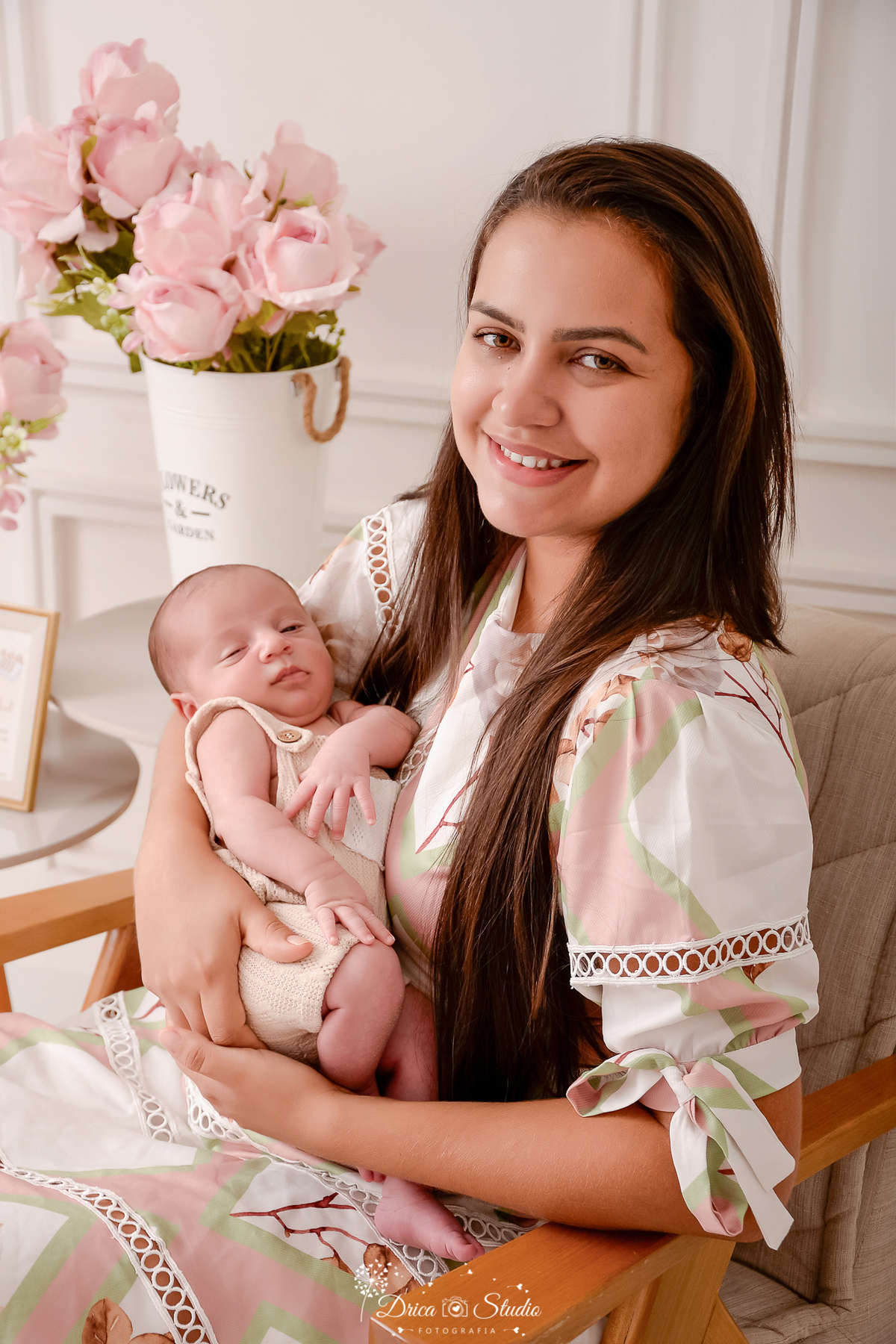 drica studio - ensaio fotografico infantil - ensaio recém-nascido - newborn - mãe segurando bebê recém-nascido, sentanda em poltrona clara com detalhes em madeira - vaso branco com flores - fundo com boiserie