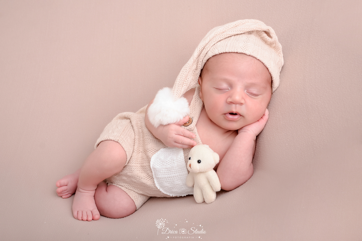 drica studio - ensaio fotografico infantil - ensaio recém-nascido - newborn - bebê recém-nascido dormindo sobre superficie macia- usando bory e gorro bege claro- ursinho branco - fundo bege