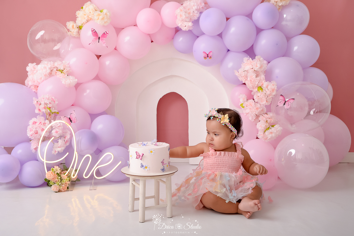 drica studio - ensaio fotográfico infantil - smash the cake - tema jardim de borboletas - xinguara - pará - balões lilas e rosa - one de led - flores e borboletas rosas - vestido e tiara rosa - bolo branco - fundo rose - painel branco