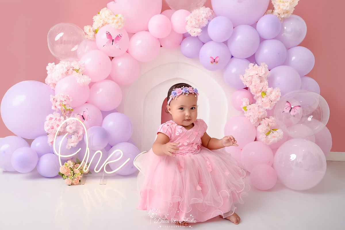 drica studio - ensaio fotográfico infantil - smash the cake - tema jardim de borboletas - xinguara -  balões rosa e lilas - flores rosa - one de led - bebê usando vestido rosa com saia em tule e tiara com flores na cabeça - fundo rose