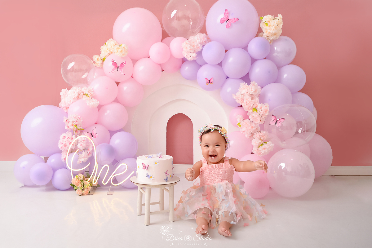 drica studio - ensaio fotográfico infantil - smash the cake - tema jardim de borboletas - xinguara - pará-bebê sentado no chão ao lado de bolo - one de led- balões rosa e lilas - flores e borboletas rosa - vestido rosa com tule e apliques de borboletas 