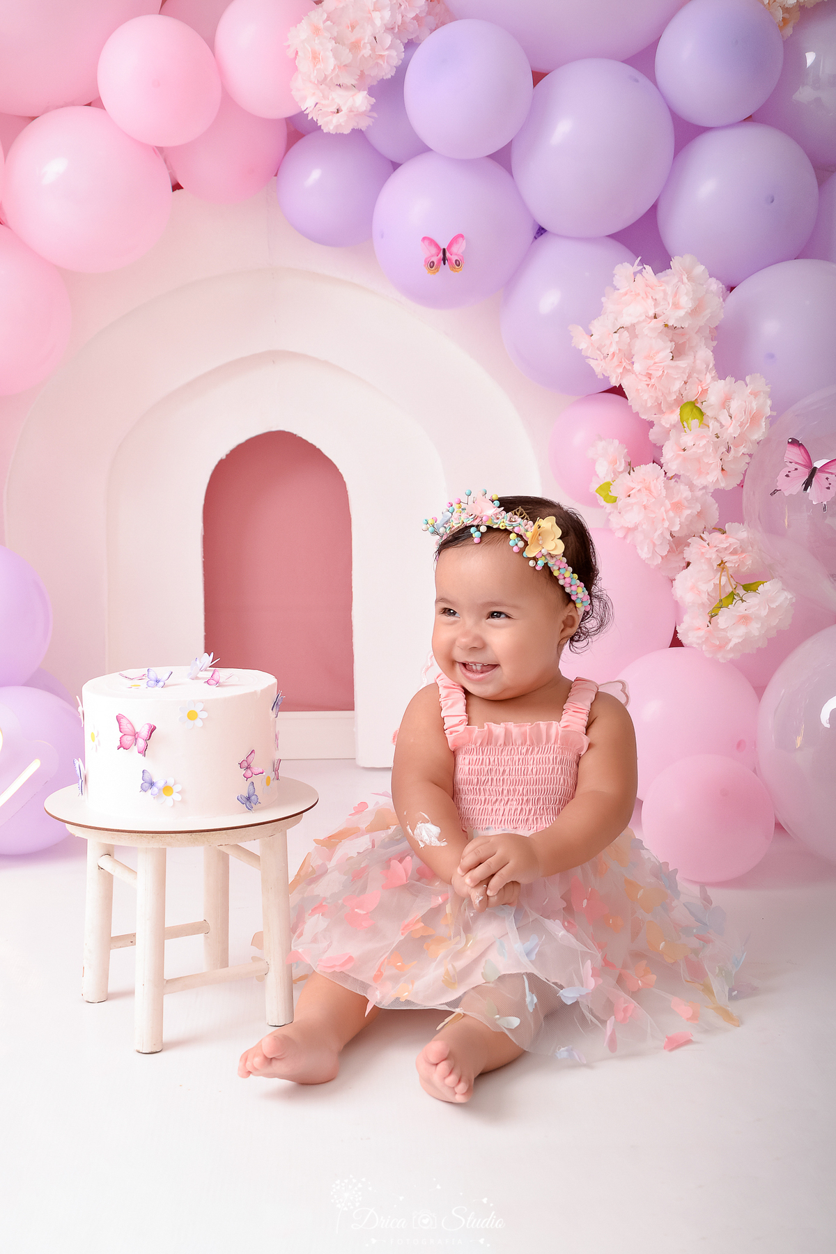 drica studio - ensaio fotográfico infantil - smash the cake - tema jardim de borboletas - xinguara - pará - bebê sentada ao lado de bolo com pequena borboletas - balões rosa e lilas - flores rosa - vestido e tiara de cabeça rosa com aplique de borboleta