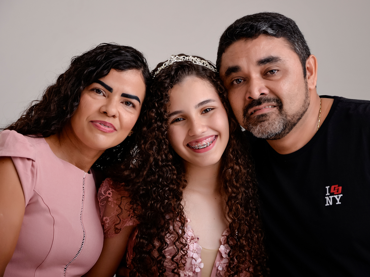 drica studio - ensaio fotografico - debutante 15 anos - aniversário - casal fazendo pose com a filha debutante - mãe e menina veste vestido rose, pai veste camiseta e calça preta - fundo neutro