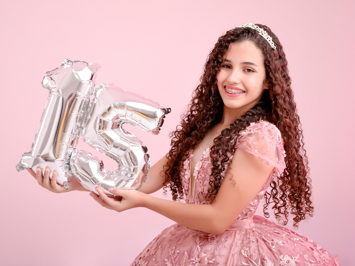 drica studio - ensaio fotografico - debutante 15 anos - aniversário - jovem debutante segurando número 15 - vestido de debutante longo na cor rose - fundo neutro