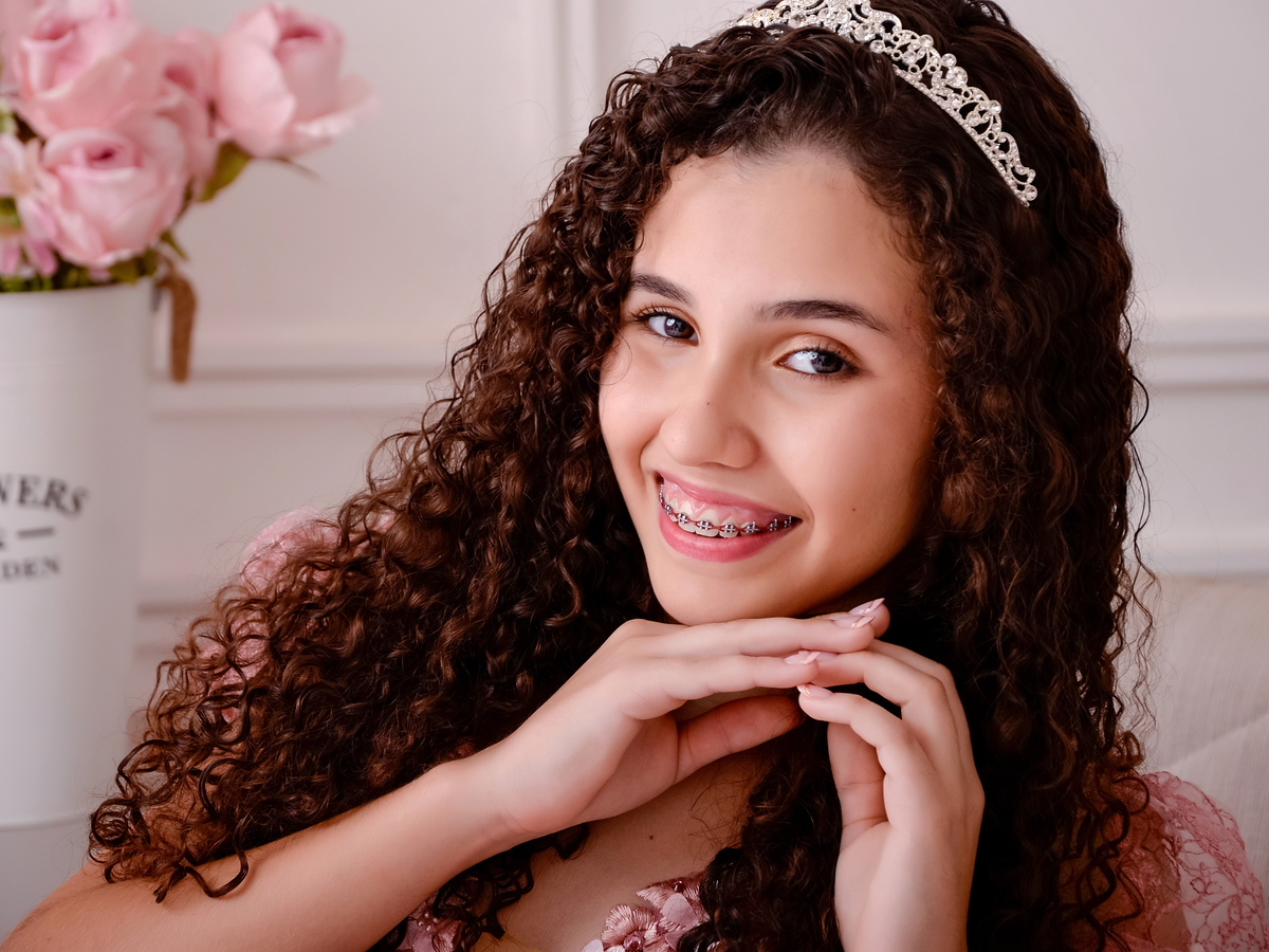 drica studio - ensaio fotografico - debutante 15 anos - aniversário - close em rosto de jovem debutante - tiara de princesa - fundo branco com boiserie - vaso com flores rosa