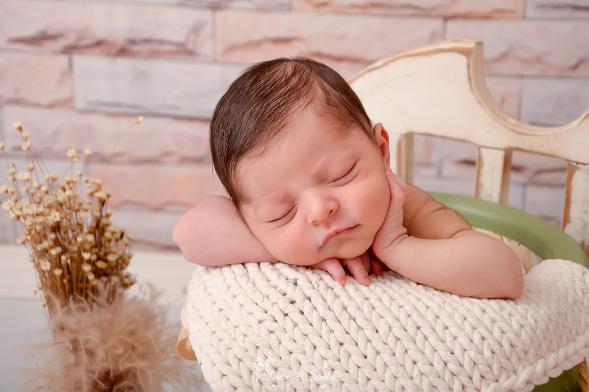 drica studio - ensaio fotografico infantil - recém-nascido - newborn masculino - recém-nascido dormindo dentro de baldinho acochoado com manta bege - flores seca - parede de tijolinho 