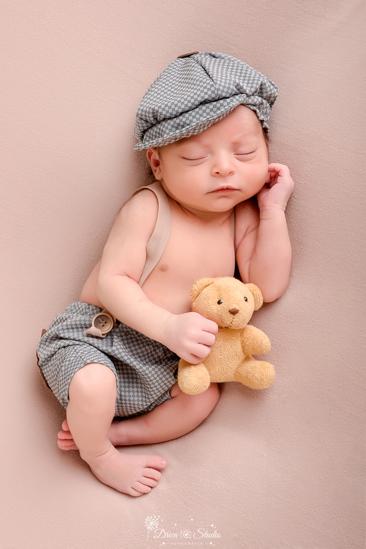 drica studio - ensaio fotografico infantil - recém-nascido - newborn masculino - recém-nascido dormindo segurando ursinho de pelucia amarelo queimado e usando apenas short cinza com suspensório - fundo neutro