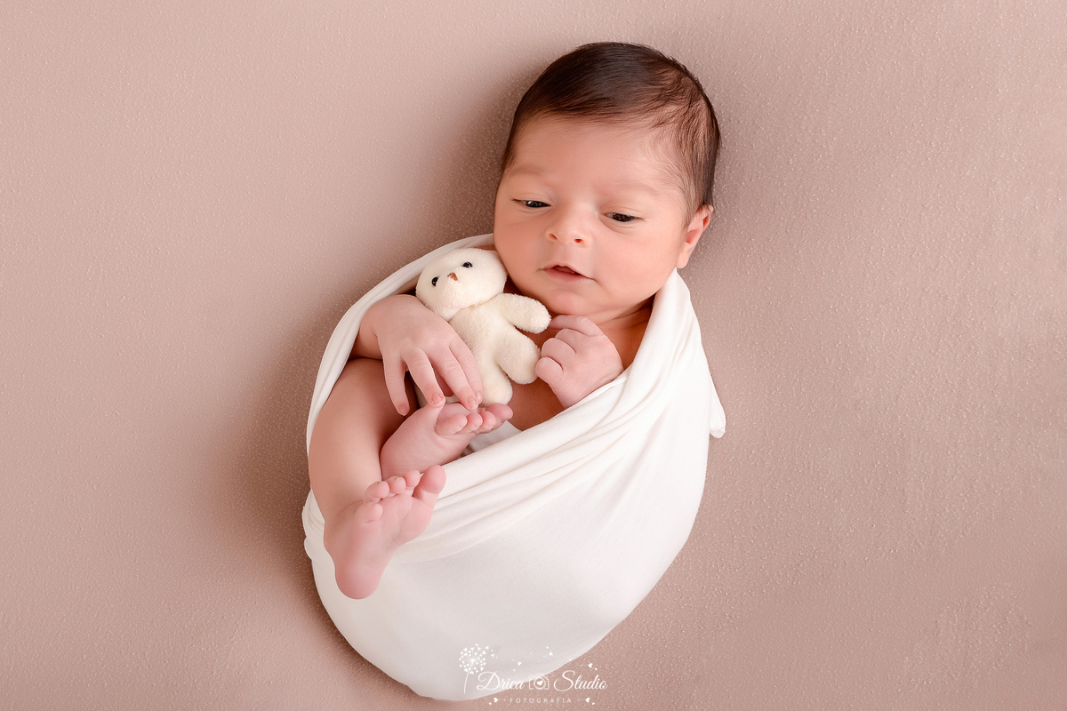 drica studio - ensaio fotografico infantil - recém-nascido - newborn masculino - recém-nascido enrolodo em manta tipo casulo com pézinho de fora, segurando ursinho branco - fundo neutro