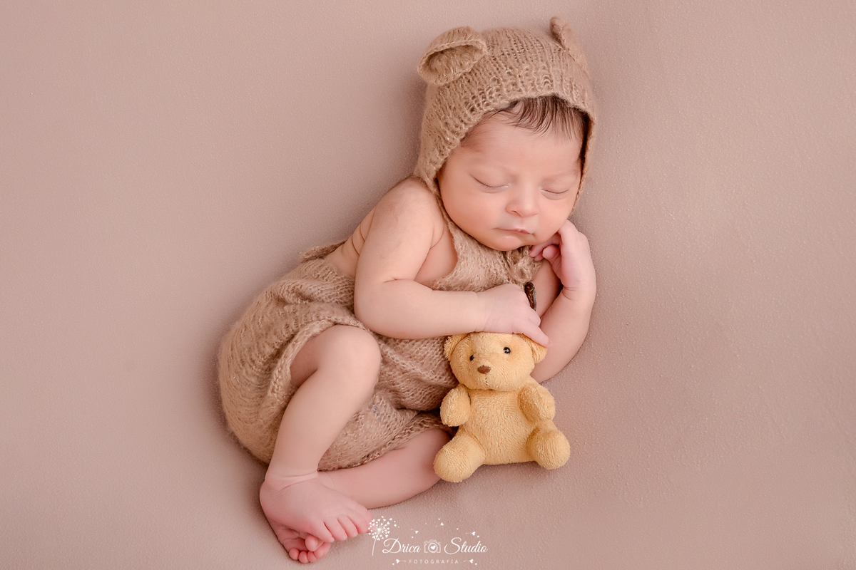 drica studio - ensaio fotografico infantil - newborn masculino - recém-nascido dormindo segurando ursinho de pelucia amarelo escuro, usando maquinho de trico bege escuro e goro com orelhas de urso - fundo neutro