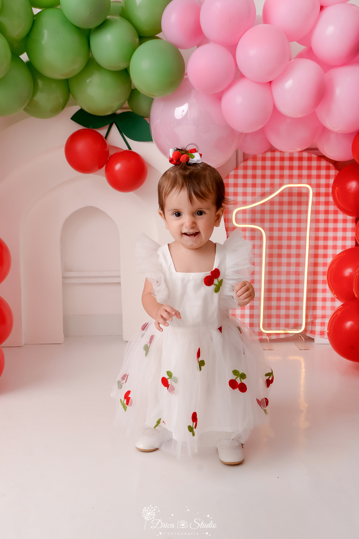 drica studio - ensaio fotografico infantil - smash the cake cerejinha - bebê sentada em banquinho, usando vestido branco com aplique de cerejinha - painel xadrez vermelho com branco - 1 de led - balões vermelho, rosa e verde - arco 3d branco