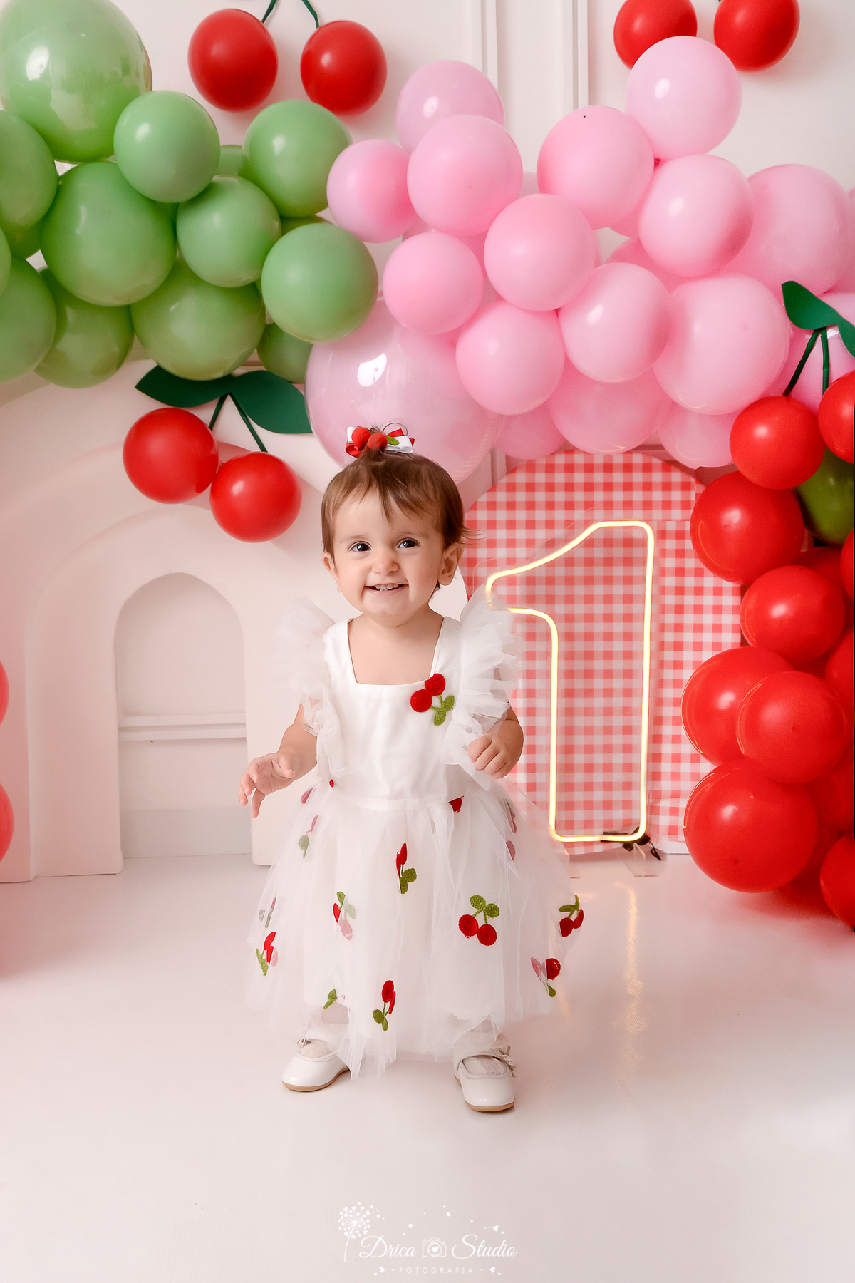 drica studio - ensaio fotografico infantil - smash the cake cerejinha - bebê usando vestido branco com aplique de cerejinha - cerejinha feitos de balão- painel xadrez vermelho e branco -1 de led- arco 3d branco - balão vermelho,verde e rosa