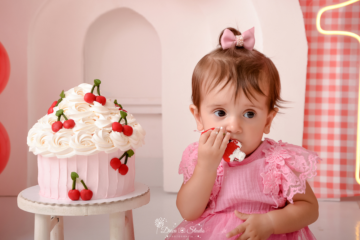 drica studio - ensaio fotografico infantil - smash the cake cerejinha -  capcake grande decorando com cerejinhas - bebê comendo bolo - bory rosa com renda - arco 3d branco - painel xadrez vermelho com branco - fundo branco