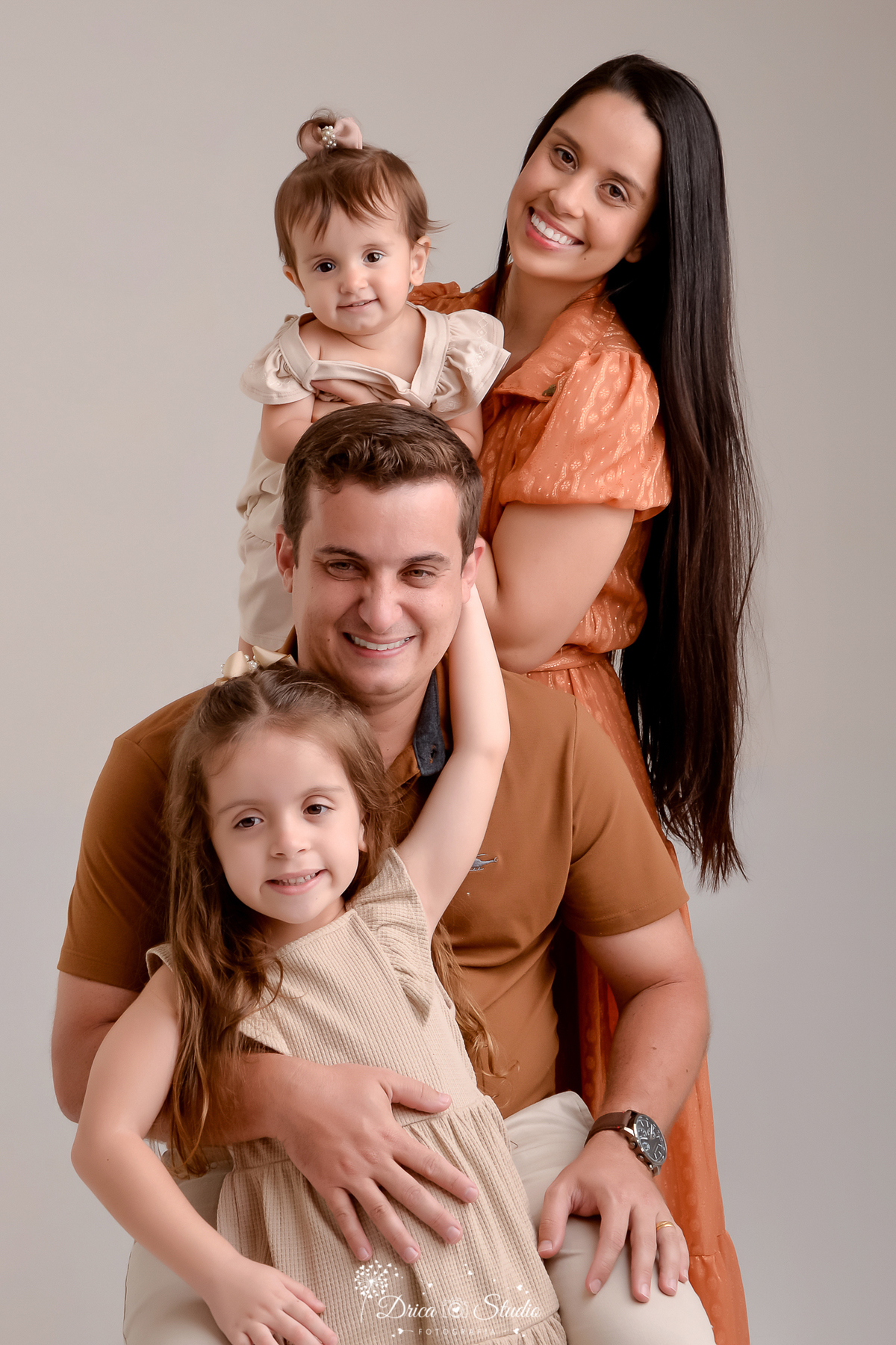 drica studio - ensaio fotografico em familia - xinguara - pará - familia posa para foto, pai sentado e a sua frente filha mais velha, atrás dele esposa com filha mais nova no colo - fundo neutro