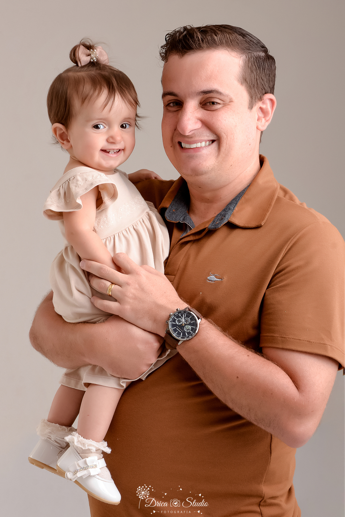 drica studio - ensaio fotografico em familia - xinguara - pará - pai posando para foto segurando filha no colo - ela veste vestido bege claro e ele camisa marrom - fundo neutro