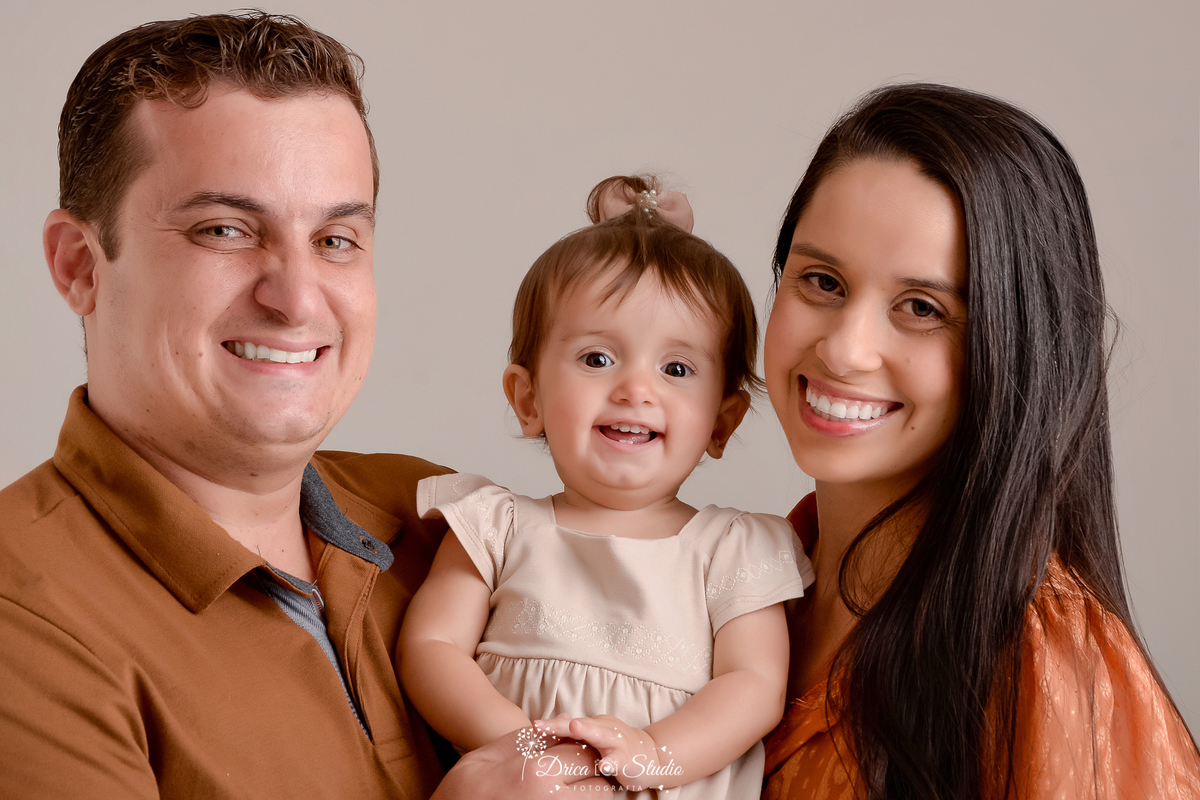 drica studio - ensaio fotografico em familia - xinguara - pará  - casal posam para foto segurando filha bebê no colo - mãe usa vestido terroso, pai camisa marrom e bebe vestido bege claro