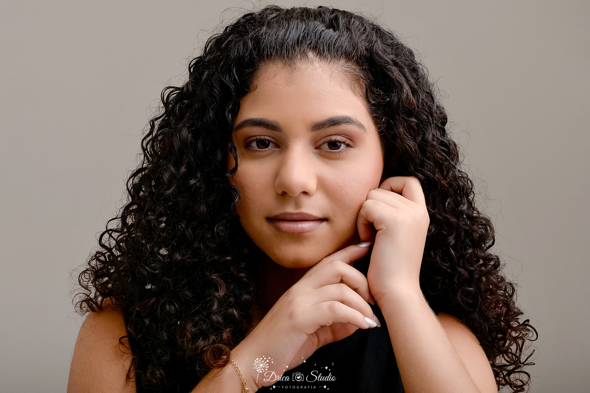 drica studio - ensaio fotografico - 15 anos - debutante - xinguara - pará - close de rosto de jovem com mãos próximo ao rosto - cabelos cacheados - fundo neutro