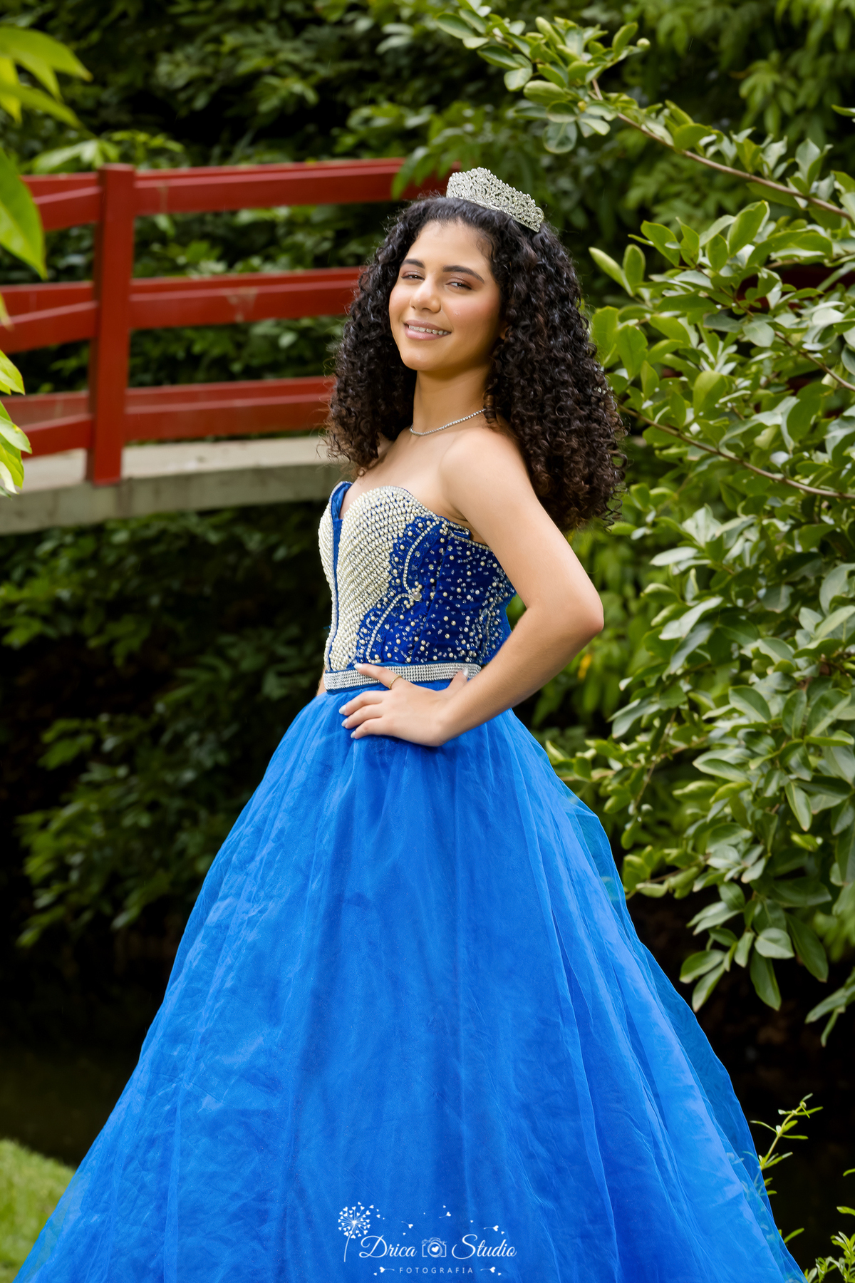 drica studio - ensaio fotografico - 15 anos - debutante - xinguara - pará ensai ao ar livre - jovem usa vestido estilo princesa azul - ela posa para fotos em jardim tropical com passarela ao fundo 