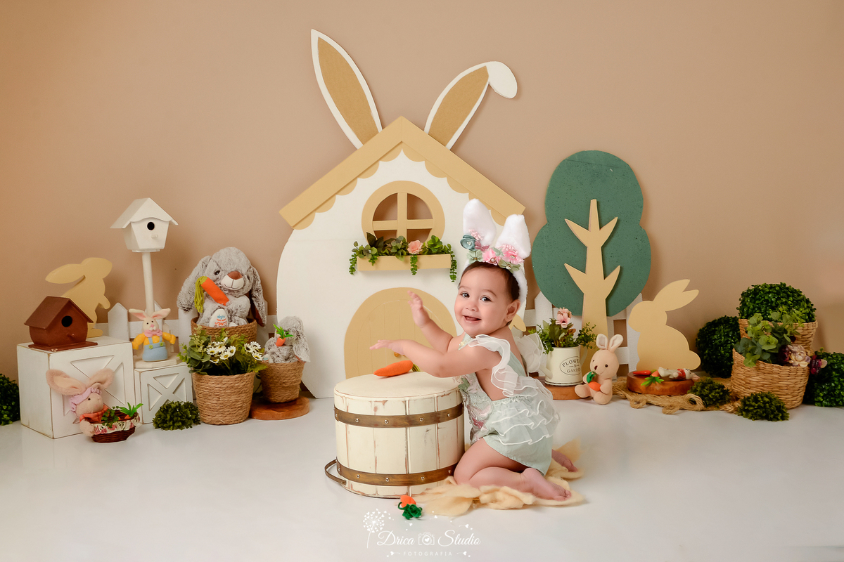 drica studio - ensaio fotografico - acompanhamento mensal - ensaio infantil páscoa - xinguara - pará - bebé de joelho proximo a balde branco - caixotes branco - casa de passarinho - coelhos de pelucia - casinha banca com orelhas de coelho -cestos de palha
