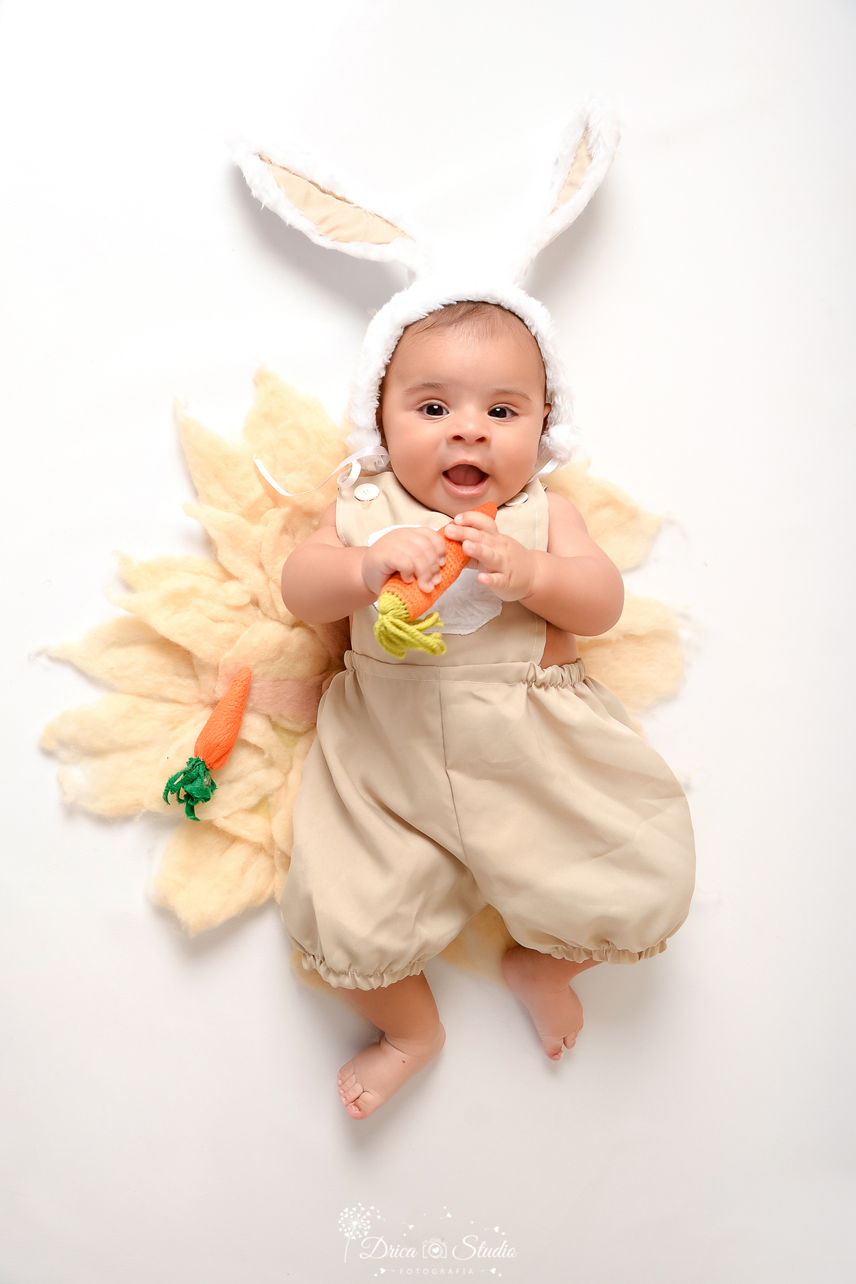 drica studio - ensaio fotografico - acompanhamento mensal - ensaio infantil páscoa - xinguara - pará - bebê deitado e barriga para cima sobre tapete felpudo, segurando uma cenoura - fundo neutro
