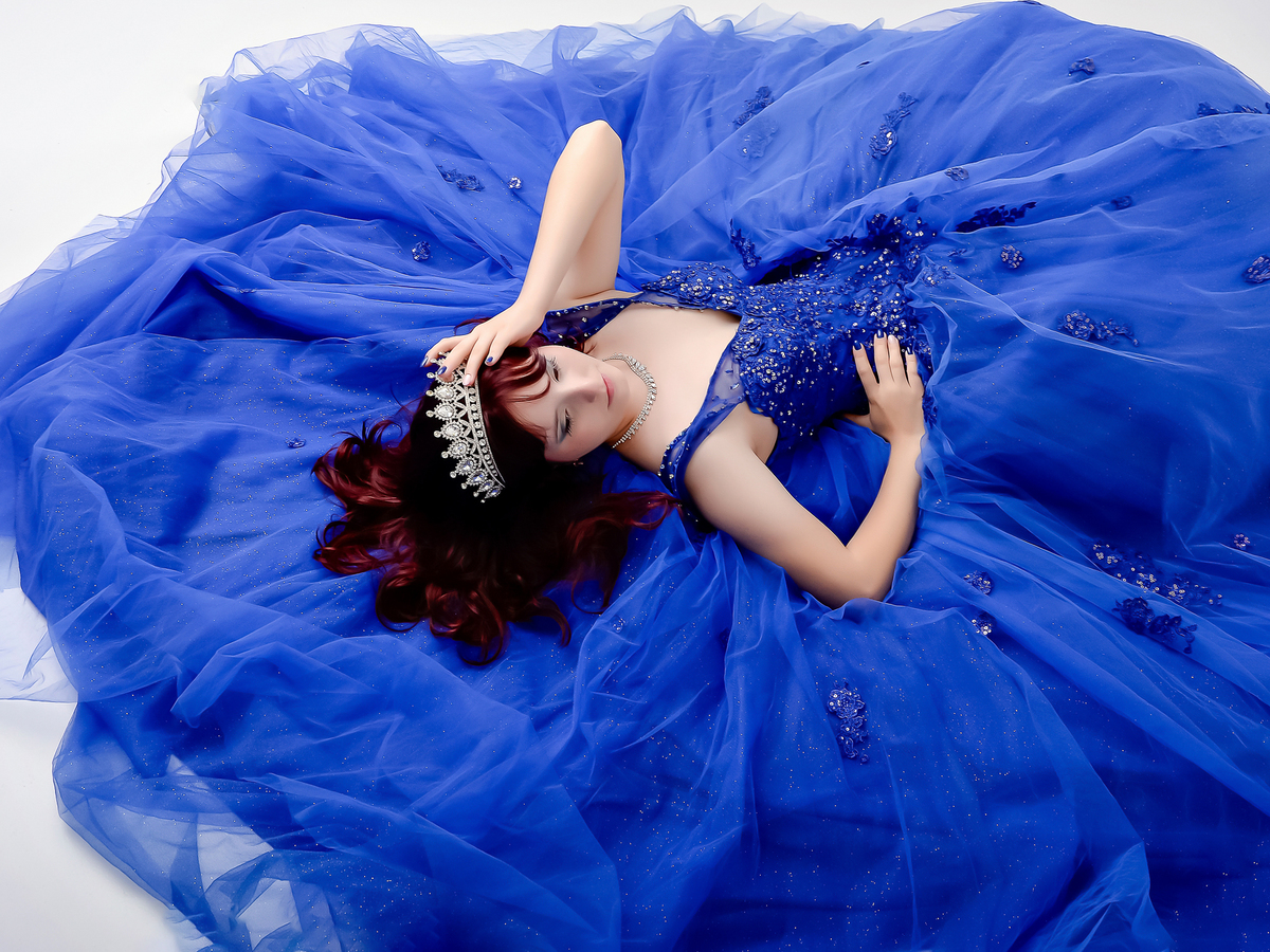 drica studio - fotos 15 anos - aniversario - debutante - vestido azul - deitada sobre o vestido - usando coroa - com as mães sobre a coroa 