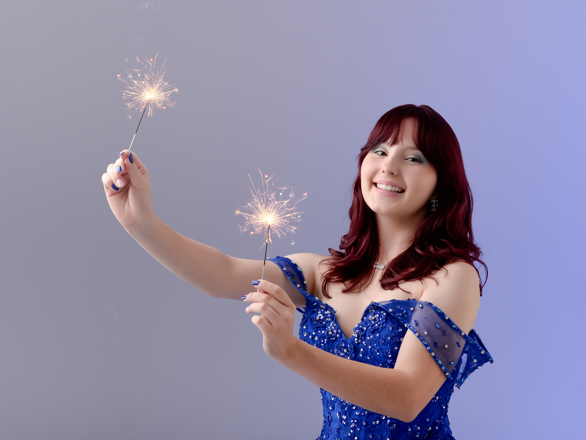 drica studio - fotos 15 anos - aniversario - debutante - estúdio - vestido azul com pedrarias - segurando duas velas acesas - sorrindo -  luz de fundo levemente azul 