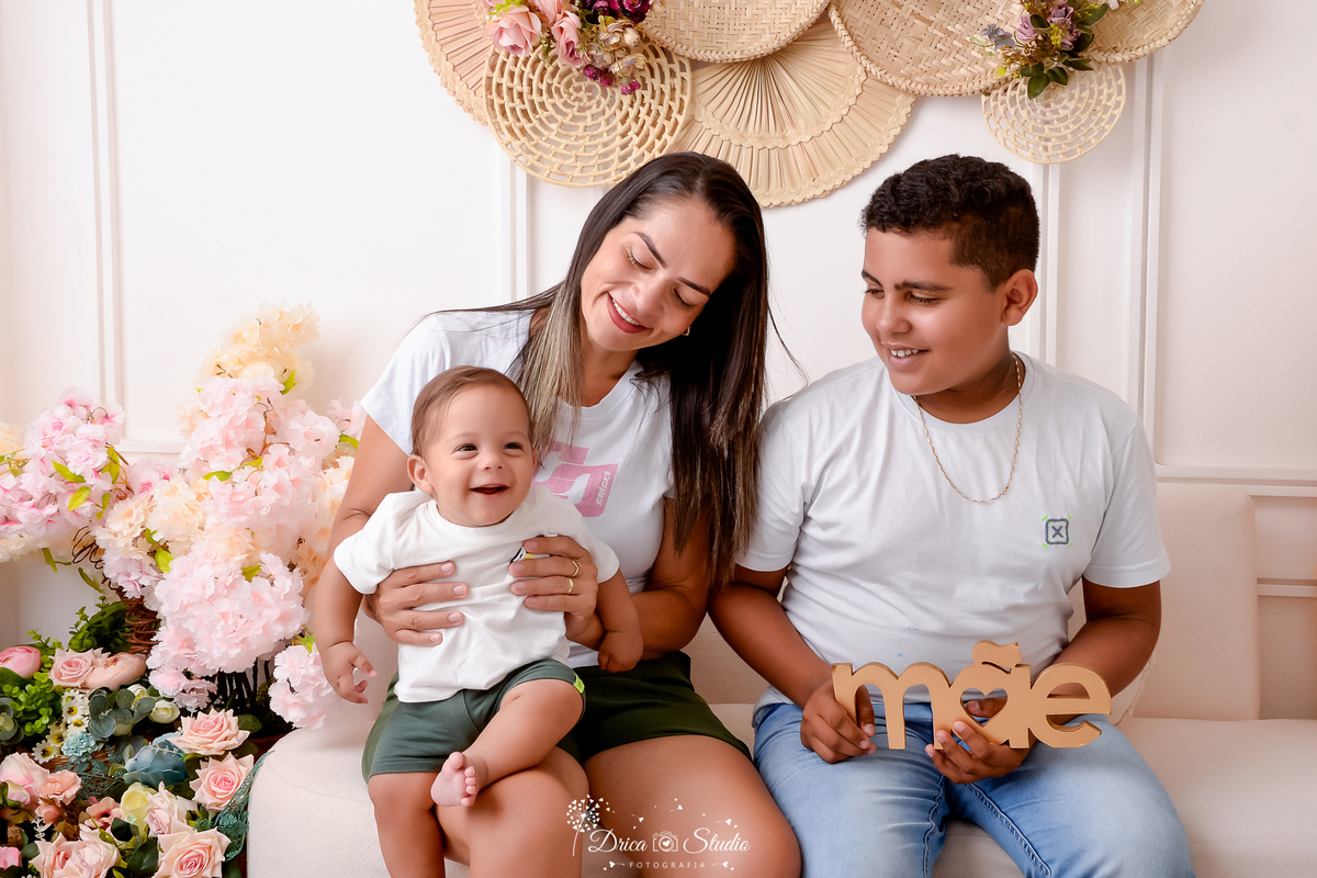 familia reunida - cenário com flores - bebê sorrindo - mãe e irmão olhando pro bebê - acompanhamento mensal - dia das mães 