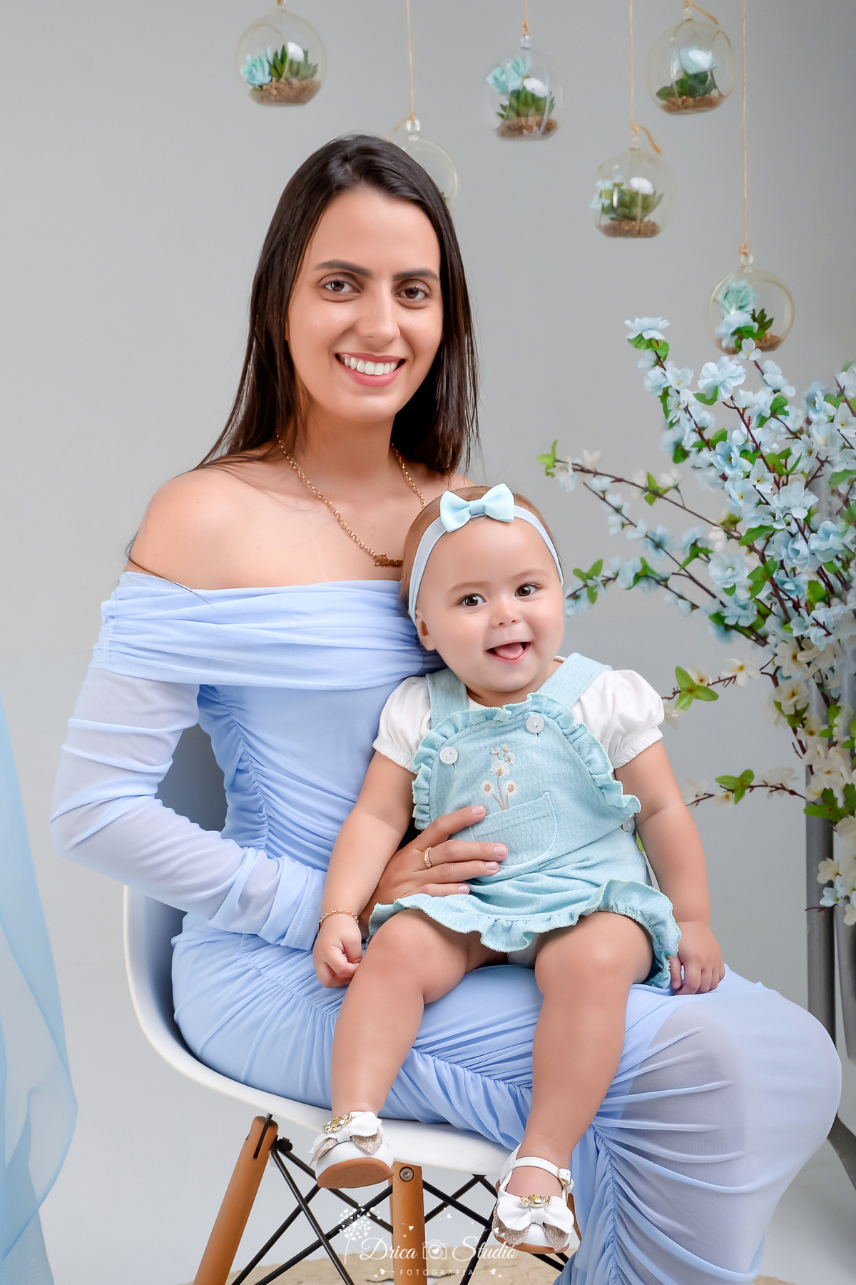 drica studio - especial de dia das mães - mães e filhos - xinguara - pará - mãe e filha usando roupas azuis - fundo com flores azuis - acompanhamento mensal - mãe e filha sorrindo olhando para a foto