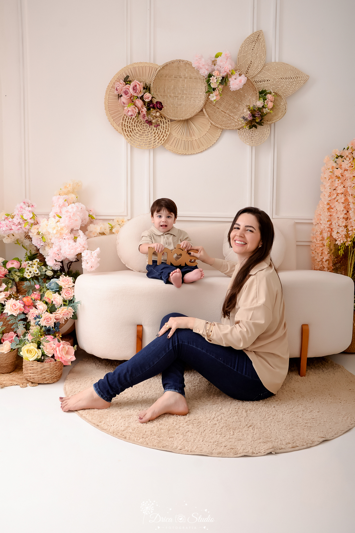 drica studio - especial de dia das mães - mães e filhos - xinguara - pará - cenário com flores - mãe e filho sorrindo - olhando para foto - bebê sentado no sofá - segurando plaquinha mãe - mamãe e bebê usando camisa nude 
