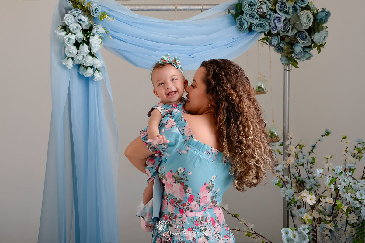 drica studio - especial de dia das mães - mães e filhos - xinguara - pará - mãe e filha - cenário azul -  com flores azuis ao fundo - mãe e filha usando vestido florado 