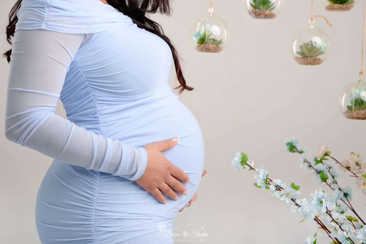drica studio - xinguara - pará - mamãe com as mãos na barriga - usando vestido azul - fundo branco -  com flores 
